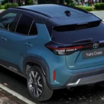 2025 Toyota Yaris Cross achteraanzicht drie-kwart met LED-achterlichten, zwarte dakspoiler en compacte SUV-proporties op stadsstraat