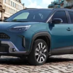 2025 Toyota Yaris Cross compacte SUV in blauwgroene metallic kleur geparkeerd op kasseistraat, vooraanzicht en zijprofiel met moderne Toyota-styling