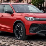 Driekwart voorkant zicht van rode 2025 Volkswagen Tiguan op kinderkopjes straat met moderne design elementen en lichtmetalen wielen