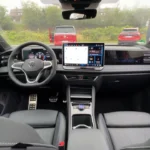 Interieurzicht van 2025 Volkswagen Tiguan met dashboard, groot touchscreen display, stuurwiel en zwarte stoelen met blauwe siernaad