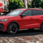 Rode 2025 Volkswagen Tiguan gefotografeerd vanuit voorkwart hoek op kinderkopjes met historische Europese architectuur op de achtergrond