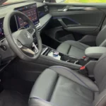 Voorstoel zicht van 2025 Volkswagen Tiguan interieur met grijze leren stoelen, middenconsole met draaiknoppen-versnellingspook en blauwe details