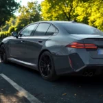 Achter driekwart aanzicht van 2025 BMW M5 op weg met herfstbomen met complete achterontwerp, achterlichten en sedan proporties