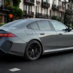 2025 BMW M5 luxe prestatie sedan in grijze metallic lak geparkeerd op stadsstraat met achter driekwart hoek met zwarte wielen en moderne achterlichten