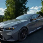 2025 BMW M5 prestatie sedan in grijze metallic op landweg met voor driekwart aanzicht met grote niergrille en sportieve bodykit