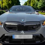 Vooraanzicht van 2025 BMW M5 met grote zwarte niergrille met M5-badge, LED-koplampen en BMW-logo op grijze metallic motorkap