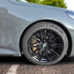 Close-up van 2025 BMW M5 zwarte lichtmetalen wiel met Michelin band, BMW naafkap en prestatie remklauw zichtbaar achter spaken