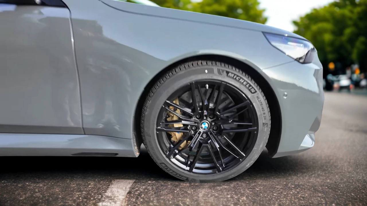 Close-up van 2025 BMW M5 zwarte lichtmetalen wiel met Michelin band, BMW naafkap en prestatie remklauw zichtbaar achter spaken