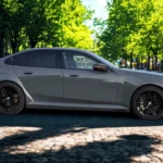 Zijprofiel aanzicht van 2025 BMW M5 op kasseienstraat met complete sedan silhouet met zwarte wielen en atletische proporties