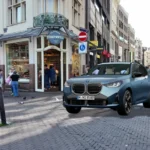 Driekwart vooraanzicht van de BMW X3 M50 uit 2025 in een stedelijke Nederlandse setting, met het nieuwe niergrille-ontwerp en LED-koplampen