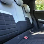 Achterpassagiers gebied van 2025 Citroën ë-C3 met gewatteerde stoelbekleding in grijs en zwart, verstelbare hoofdsteunen en ruim interieur met raamzicht