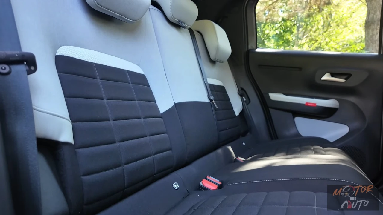 Achterpassagiers gebied van 2025 Citroën ë-C3 met gewatteerde stoelbekleding in grijs en zwart, verstelbare hoofdsteunen en ruim interieur met raamzicht