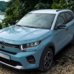 Lichtblauwe 2025 Citroën ë-C3 elektrische crossover in schilderachtige omgeving met water en bomen op achtergrond, moderne LED-koplampen, zwarte kunststof bekleding en geometrische lichtmetalen velgen tonend