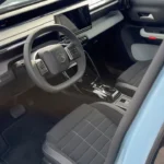 Voor interieurbeeld van 2025 Citroën ë-C3 elektrische auto met grijs dashboard, Citroën stuurwiel, gewatteerde stoelbekleding en moderne interieurdesign-elementen