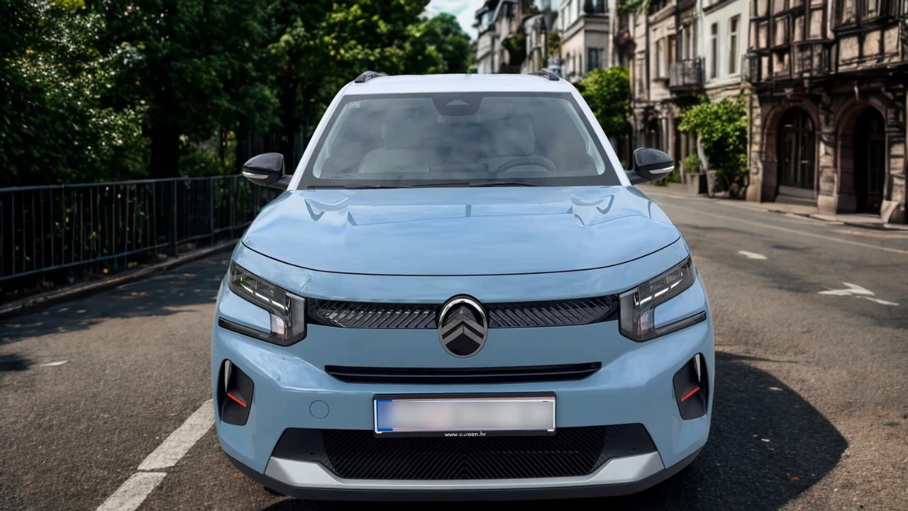 Vooraanzicht van lichtblauwe 2025 Citroën ë-C3 elektrische auto op Europese stadsstraat met historische gebouwen op achtergrond, LED-koplampen, chevron-grille en compacte crossover-proporties tonend
