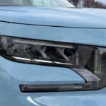 Gedetailleerd beeld van 2025 Citroën ë-C3 LED-koplamp met moderne lichtsignatuur, dagrijverlichting en strak design geïntegreerd in het lichtblauwe carrosseriepaneel