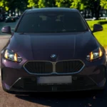 2025 BMW 1 Serie vooraanzicht met verlichte LED-koplampen met oranje dagrijverlichting, grote BMW niergrille en agressief voorbumper ontwerp in paarse metallic