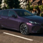 2025 BMW 1 Serie compacte hatchback in paarse metallic lak geparkeerd op een met bomen omzoomde straat, driekwart vooraanzicht met karakteristieke BMW niergrille en LED-koplampen