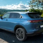 2025 Honda HR-V driekwart achterzicht tegen schilderachtig landschap met glooiende heuvels, wat het avontuur-klare ontwerp en blauwe buitenafwerking van de SUV demonstreert.