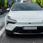 Directe vooraanzicht van witte 2025 Polestar 4 op stedelijke straat met volledige voorkant met LED-koplampen, gesloten grille-ontwerp en Polestar-sterlogo op motorkap