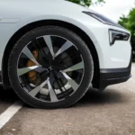 Close-up van het voorwiel van de 2025 Polestar 4 met zilveren lichtmetalen velg met zwarte spaken, gele remklauw en Polestar 4-badge op witte elektrische auto carrosserie