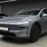 Voorkwart aanzicht van de nieuwe Tesla Model Y in zilver, gepositioneerd in showroom naast blauwe Model Y, met focus op het herontworpen front