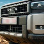 Close-up van 2025 Toyota Land Cruiser voorkant tonend kenmerkende zwarte grille met TOYOTA letters en moderne LED koplamp units