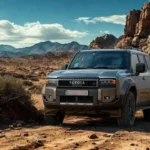 Zijprofiel aanzicht van grijze 2025 Toyota Land Cruiser gepositioneerd in woestijn setting met dramatische rotsachtige bergen en bewolkte lucht op achtergrond