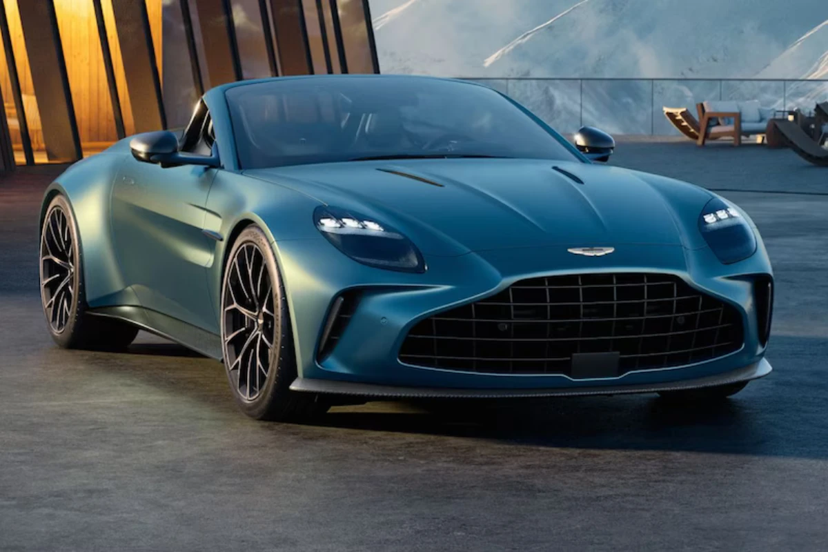 De 2025 Aston Martin Vantage Roadster toont zijn kenmerkende grille en aerodynamisch ontwerp tegen een moderne architecturale achtergrond