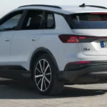 Witte Audi Q4 40 e-tron gefotografeerd vanuit achterkwartier hoek met zijn gestroomlijnd achterlichtdesign en two-tone carrosserie met zee op de achtergrond