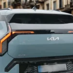 Witte 2025 Kia EV3 elektrische SUV van achteren, met oranje LED-achterlichten, KIA-logo en EV3-badge op historische Europese kasseienstraat