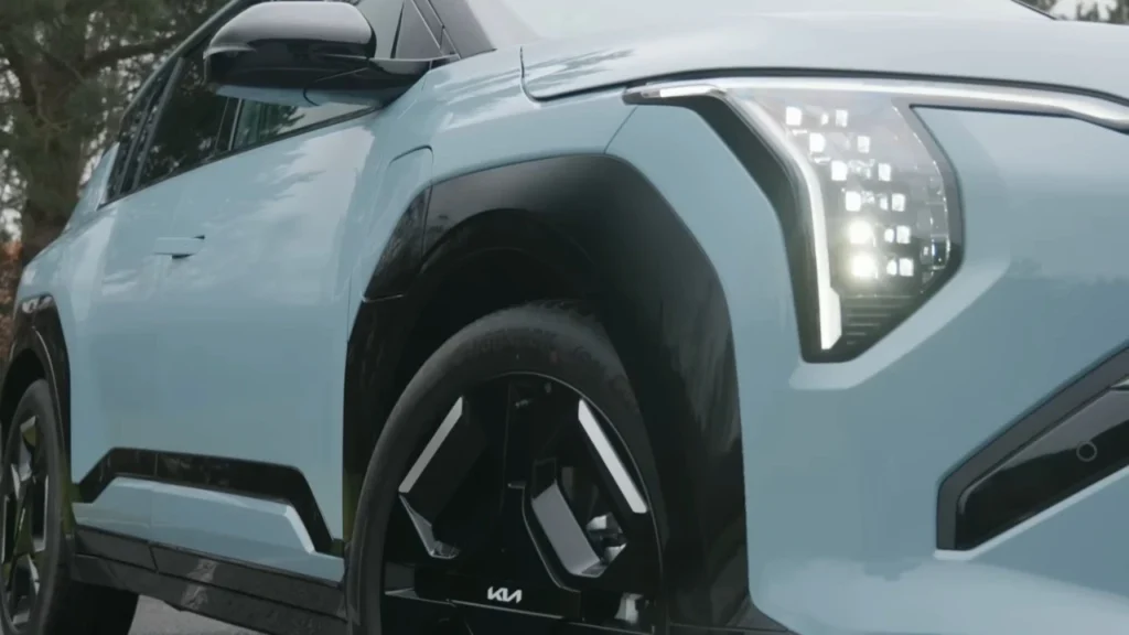 Close-up detail opname van lichtblauwe 2025 Kia EV3 met LED-koplamp cluster, voorwiel met KIA-logo en modern voorbumperontwerp
