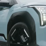 Close-up detail opname van lichtblauwe 2025 Kia EV3 met LED-koplamp cluster, voorwiel met KIA-logo en modern voorbumperontwerp