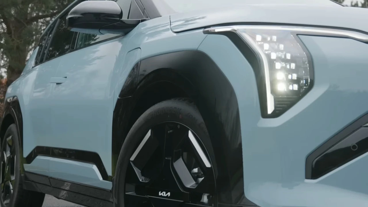 Close-up detail opname van lichtblauwe 2025 Kia EV3 met LED-koplamp cluster, voorwiel met KIA-logo en modern voorbumperontwerp
