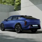 Blauwe Kia EV4 GT-Line getoond vanaf de achterkant kwartierhoek, met nadruk op zijn fastback-design, unieke achterlichtensignatuur en GT-Line specifieke stylingelementen tegen een architecturale achtergrond