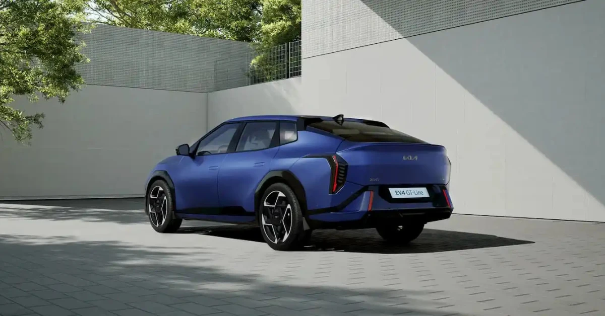 Blauwe Kia EV4 GT-Line getoond vanaf de achterkant kwartierhoek, met nadruk op zijn fastback-design, unieke achterlichtensignatuur en GT-Line specifieke stylingelementen tegen een architecturale achtergrond