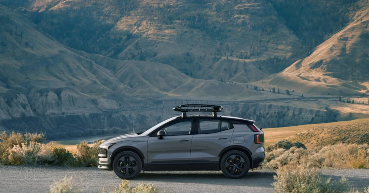 Zijaanzicht van de Volvo EX30 Cross Country geparkeerd tegen een dramatische bergachtergrond met dakdrager