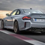 Dynamisch achter drie-kwart zicht van 2025 BMW M2 CS op circuit met koolstofvezel achterdiffuser, eendenstaart spoiler, brede achterbanden, en agressief aerodynamisch pakket in beweging