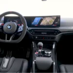Volledig interieurzicht van 2025 BMW M2 CS met koolstofvezel middenconsole, curved display schermen, M sport stuurwiel, automatische transmissie, en premium zwarte bekleding met rode accenten