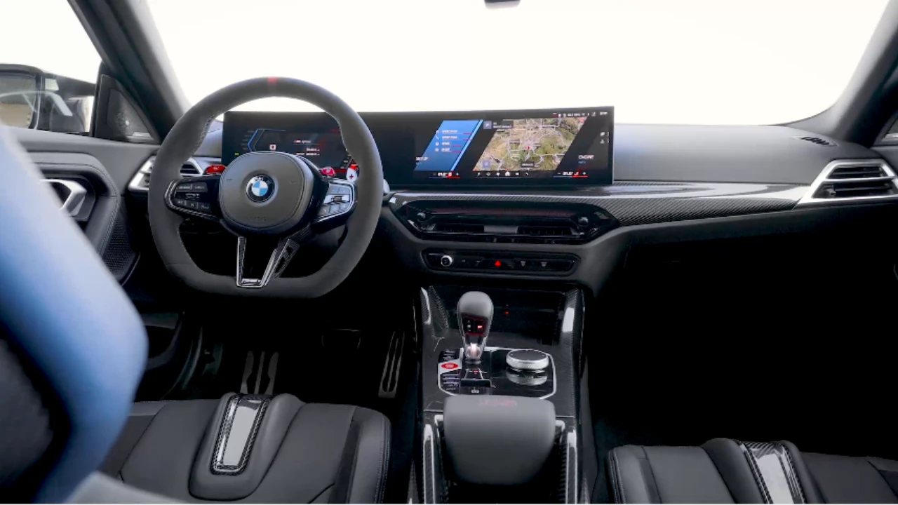 Volledig interieurzicht van 2025 BMW M2 CS met koolstofvezel middenconsole, curved display schermen, M sport stuurwiel, automatische transmissie, en premium zwarte bekleding met rode accenten