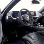 Interieurzicht van 2025 BMW M2 CS met koolstofvezel dashboard, platte M stuurwiel met rode middenmarkering, curved display schermen, en premium Alcantara bekleding
