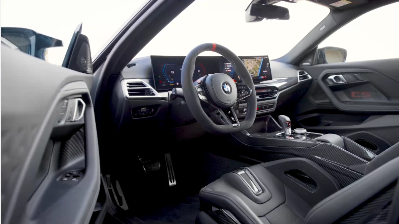 Interieurzicht van 2025 BMW M2 CS met koolstofvezel dashboard, platte M stuurwiel met rode middenmarkering, curved display schermen, en premium Alcantara bekleding