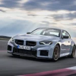 Dynamisch voor drie-kwart zicht van 2025 BMW M2 CS in zilver op racebaan, met aggressieve frontsplitter, grote niergrille, aerodynamische carrosserie, en Gold Bronze wielen