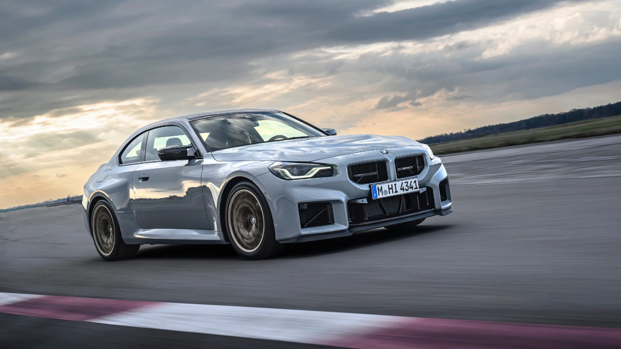 Zijaanzicht van 2025 BMW M2 CS in beweging met koolstofvezel dak, verlaagde houding, Gold Bronze gesmede wielen, circuitbanden, en aggressieve aerodynamische zijkant elementen
