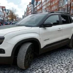 Voor driekwart hoek van witte 2025 Jeep Avenger op Europese straat toont zeven-slot grille, LED koplampen en compact stadsvriendelijk ontwerp