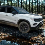 Witte 2025 Jeep Avenger compacte SUV navigeert rotsachtig bosterrein, toont off-road capaciteit met verhoogde bodemvrijheid en beschermende carrosseriebekleding