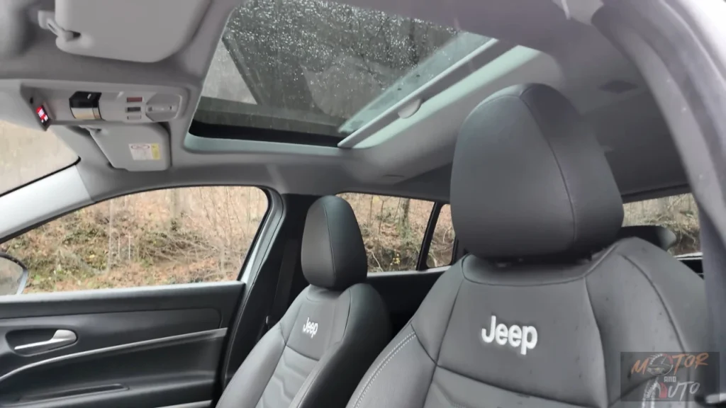 Interieur opname van 2025 Jeep Avenger toont panoramisch schuifdak opening boven voorstoelen met Jeep logo geborduurd hoofdsteunen