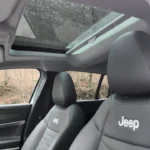 Interieur opname van 2025 Jeep Avenger toont panoramisch schuifdak opening boven voorstoelen met Jeep logo geborduurd hoofdsteunen