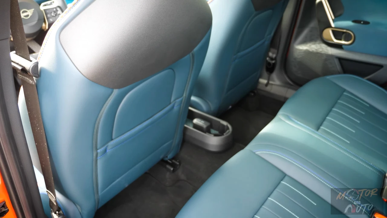 Zicht vanuit achterstoelen van Mini Aceman met beenruimte achter voorstoelen, centrale bekerhouder, USB-oplaadpoorten, en blauwe gewatteerde bekleding