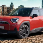 Rode 2025 Mini Aceman elektrische SUV met zwart dak, hoekige LED-koplampen, gesloten EV-grille en tweetone carrosseriebescherming geparkeerd op geplaveide straat met Europese architectuur achtergrond